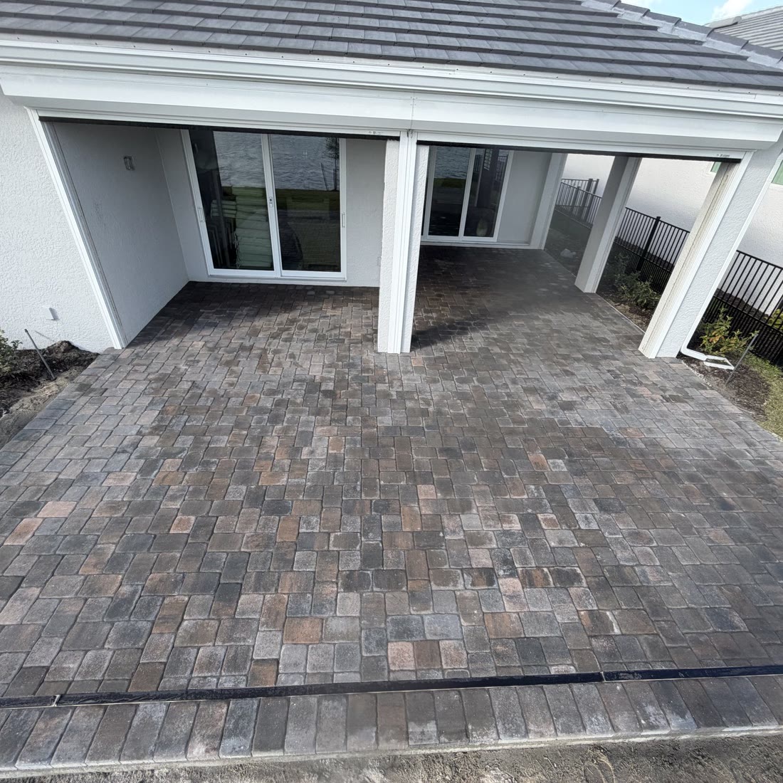 A new paver patio under a white covered lanai at the back of a house.