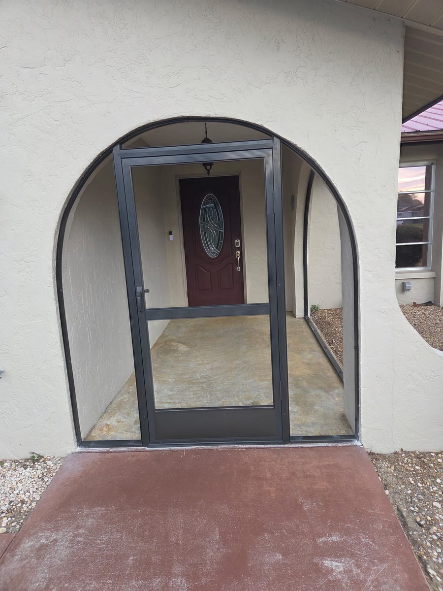 A rounded front entry closed in with a bronze screen door and screen panels.