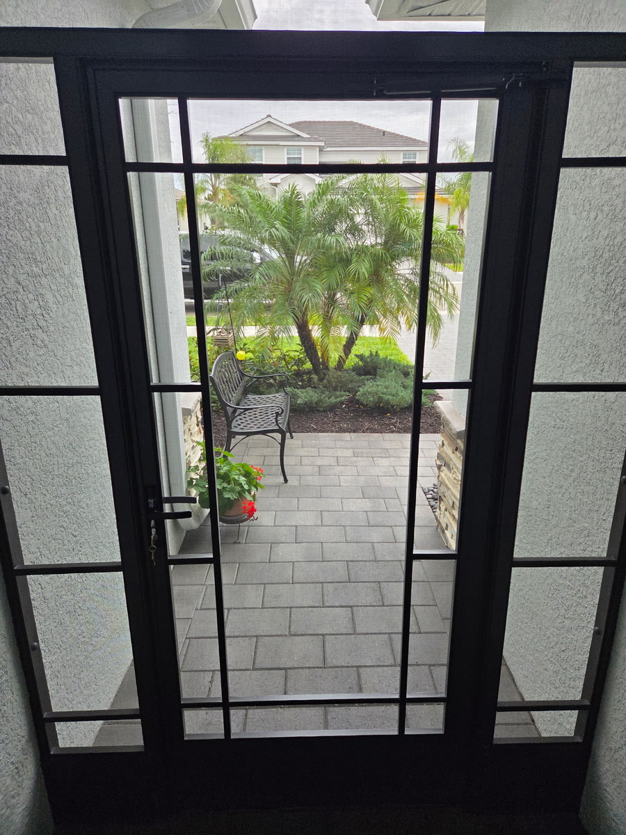 A bronze screen door looking out to a paver walk and plants.