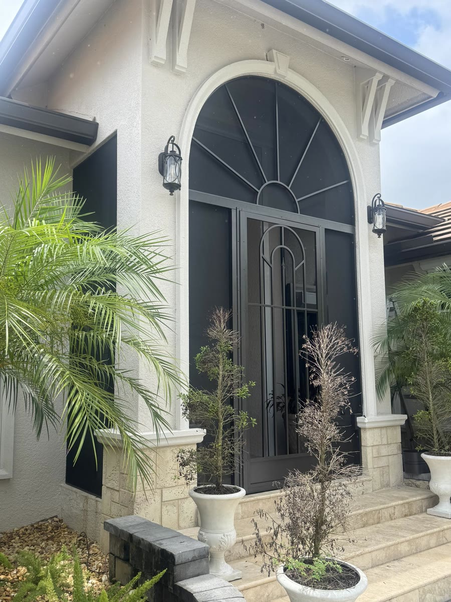 An arched front entry with a dark screen door between two potted palms.