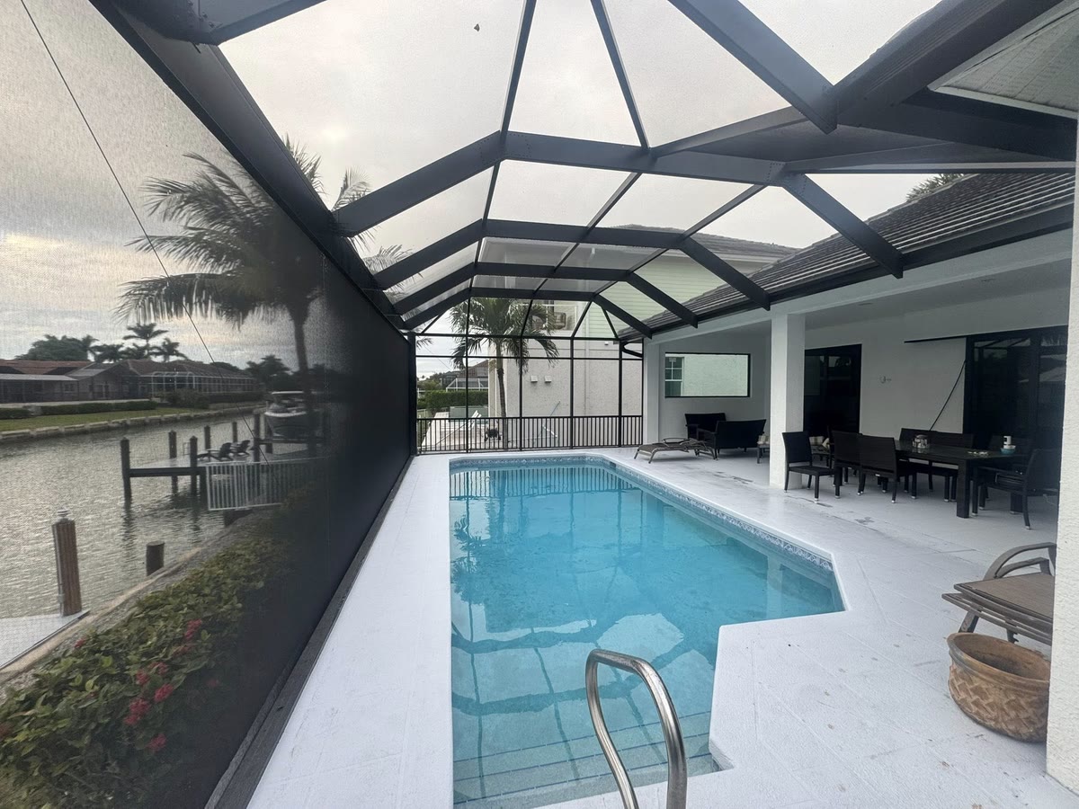 A bronze cage over a pool on a canal, the boat dock showing through the screen.