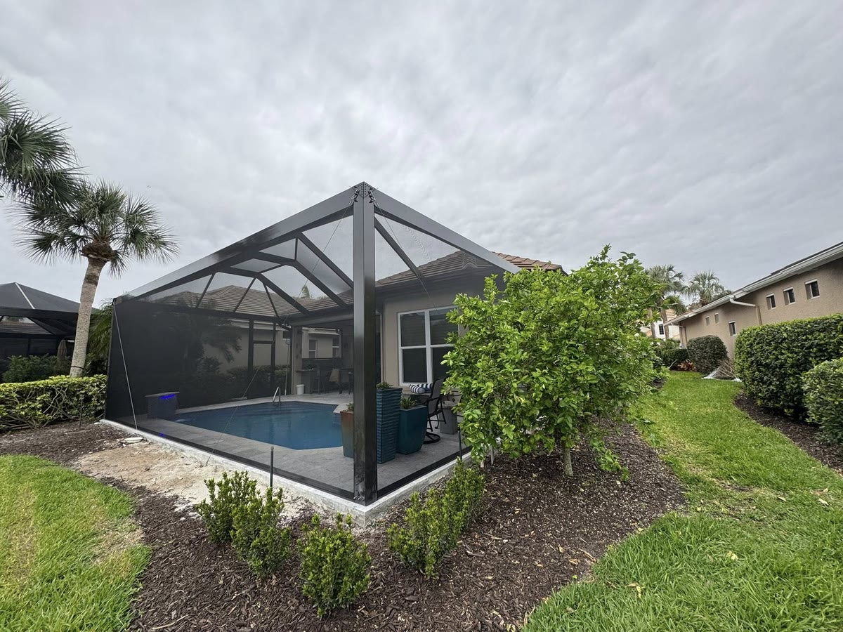 A small bronze pool cage beside a house, with new plantings around its base.