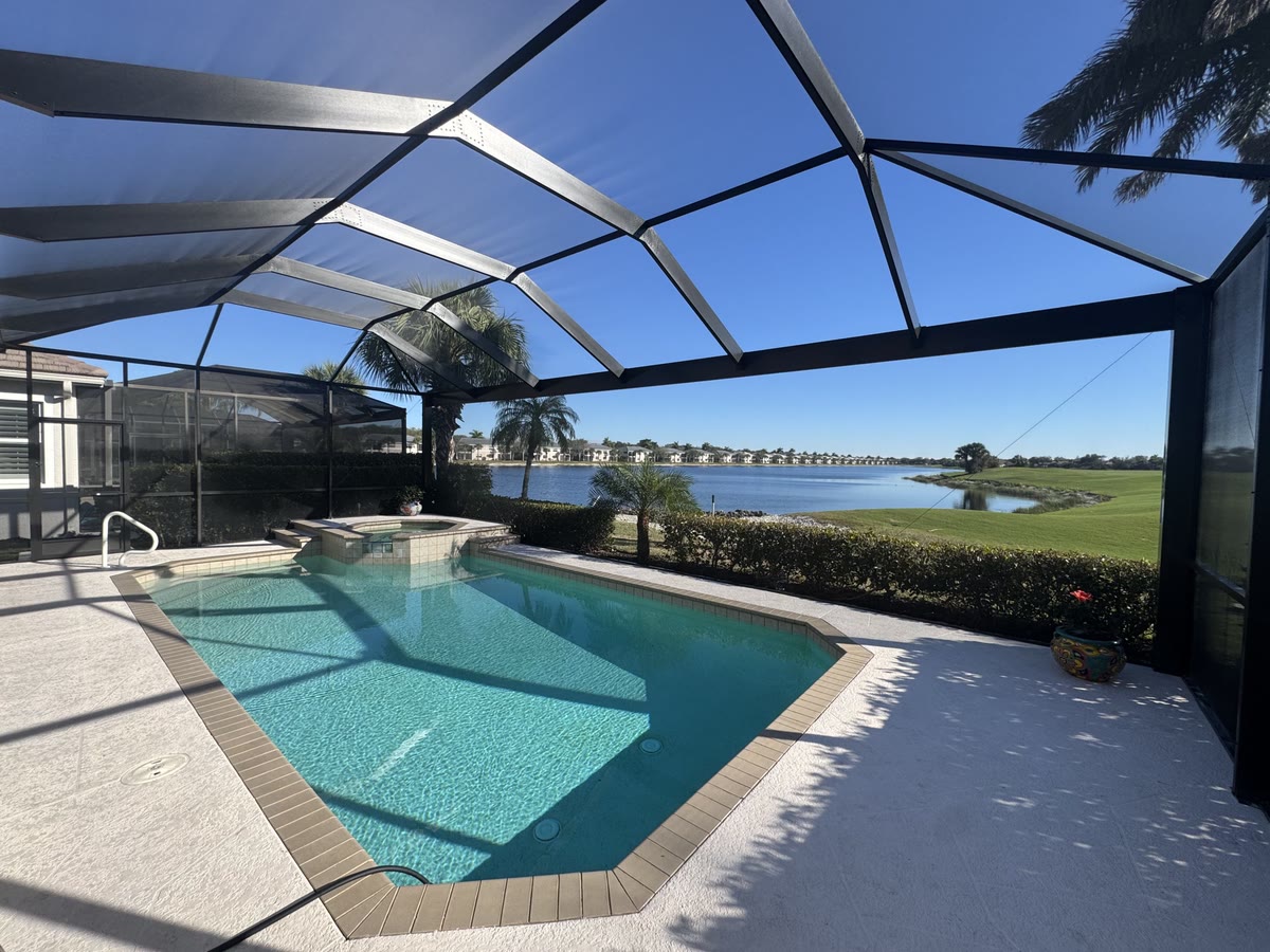 Inside a dark bronze pool cage: a pool and spa, a lake and a golf course beyond the screen.