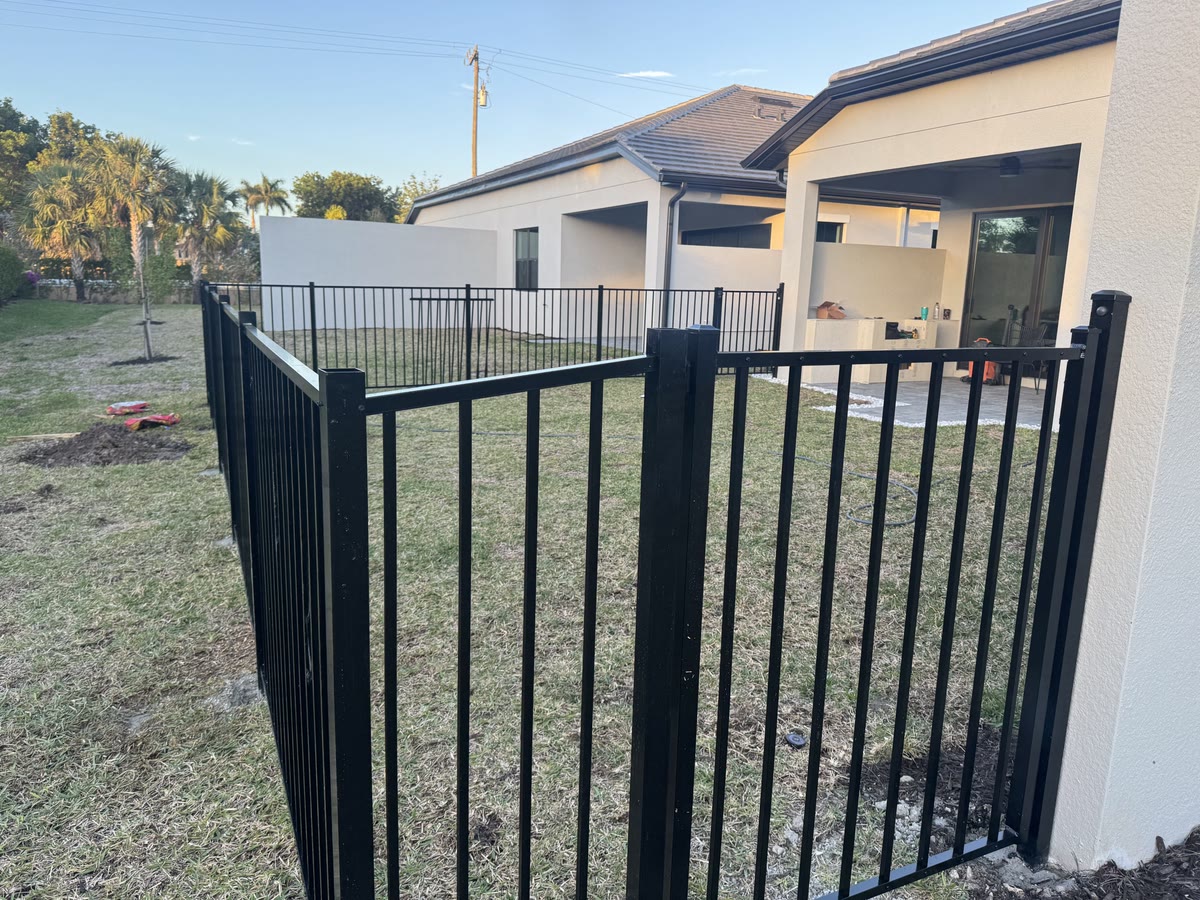 A black aluminum fence and gate in a side yard beside a new house.