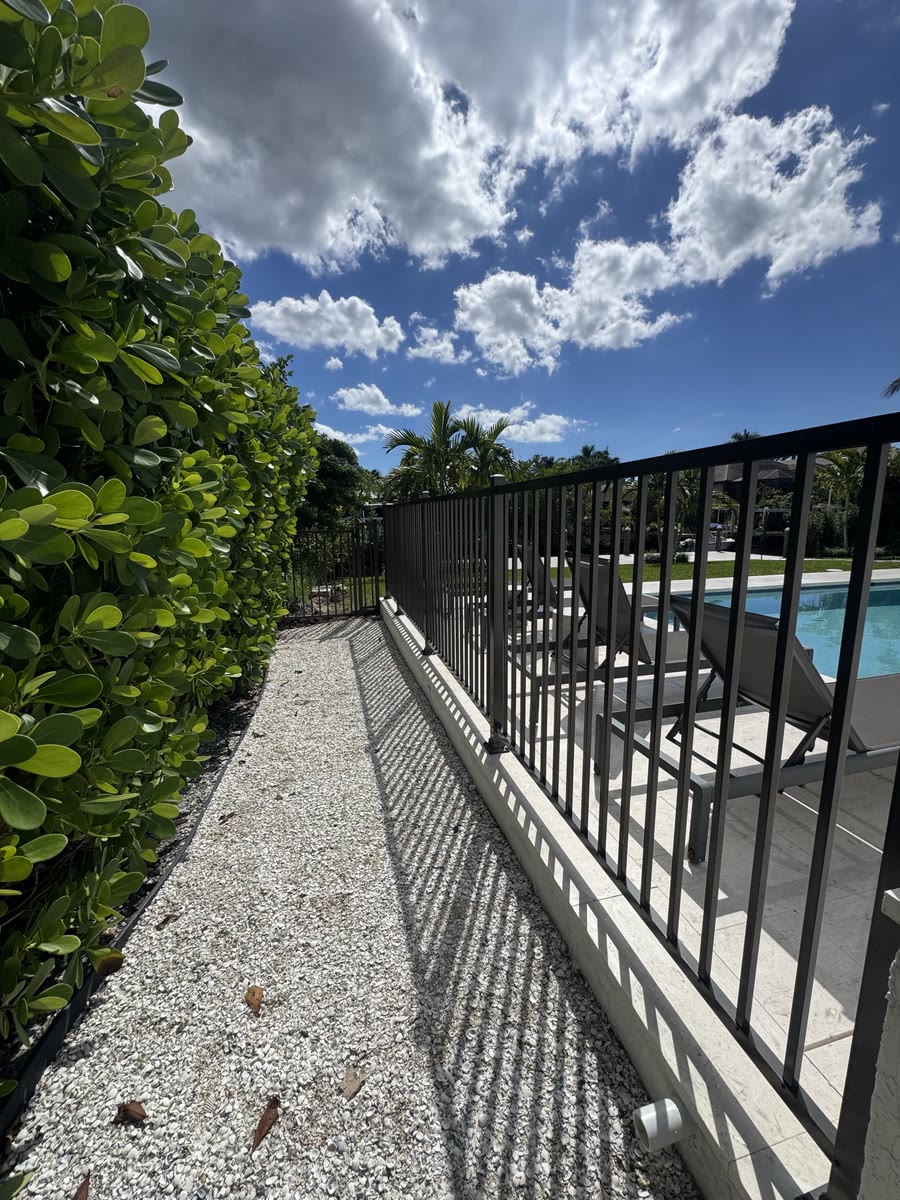 A black aluminum fence along a narrow gravel side yard.