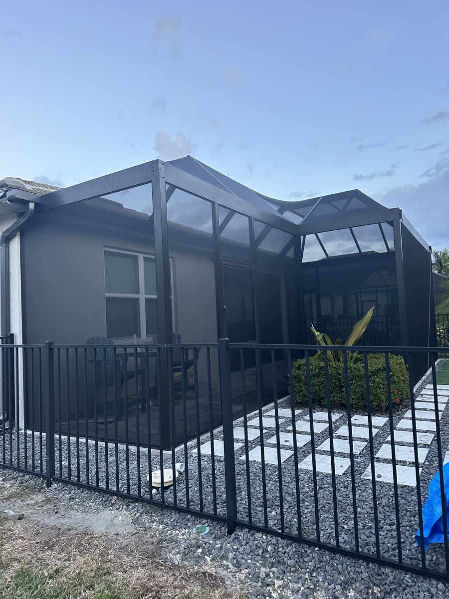 A black aluminum fence around a gravel side yard of a two-storey grey house.