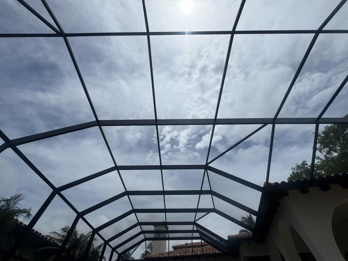 Looking up through a cage roof of new dark screen at a cloudy sky.