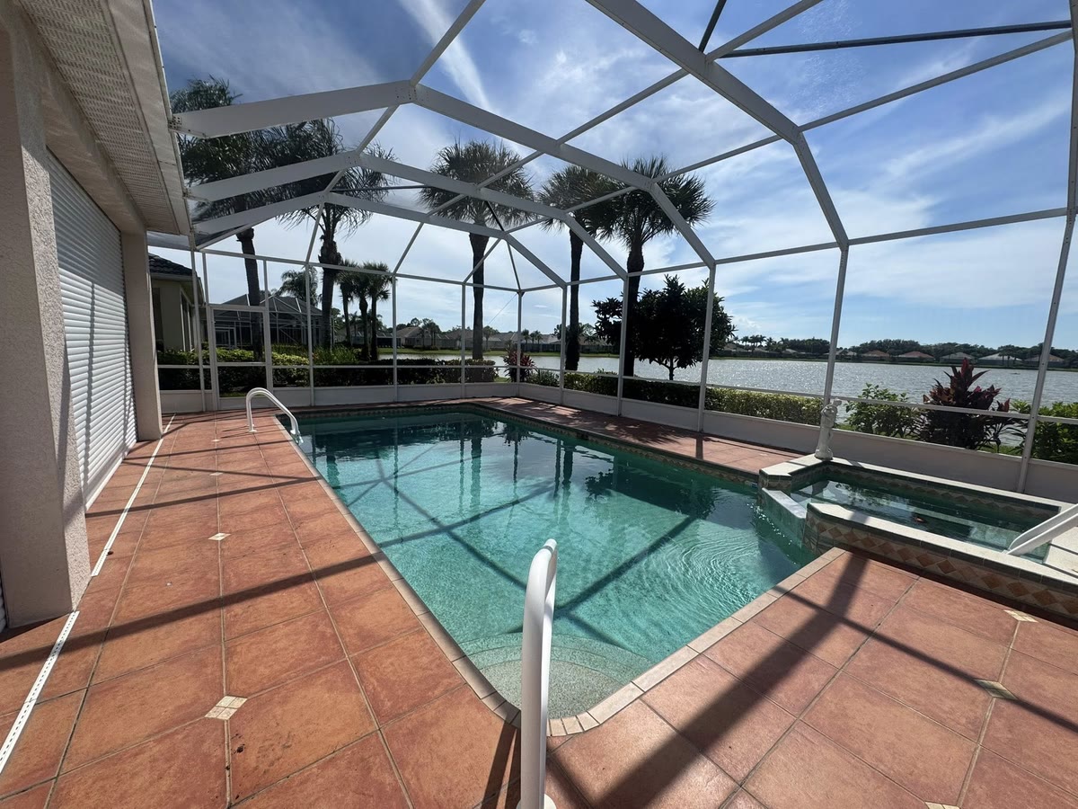 A white pool cage over a pool on a terracotta deck, a lake beyond.
