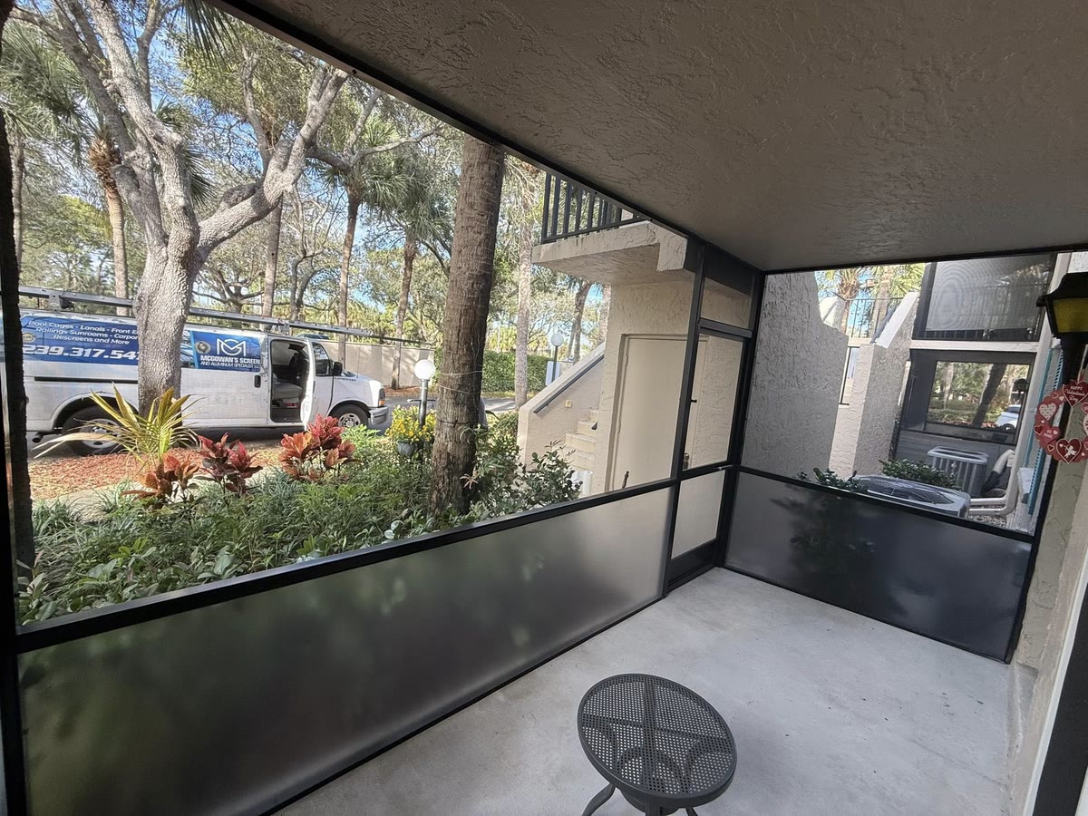 A screened ground-floor porch with dark kick panels, a work van in the lot beyond.