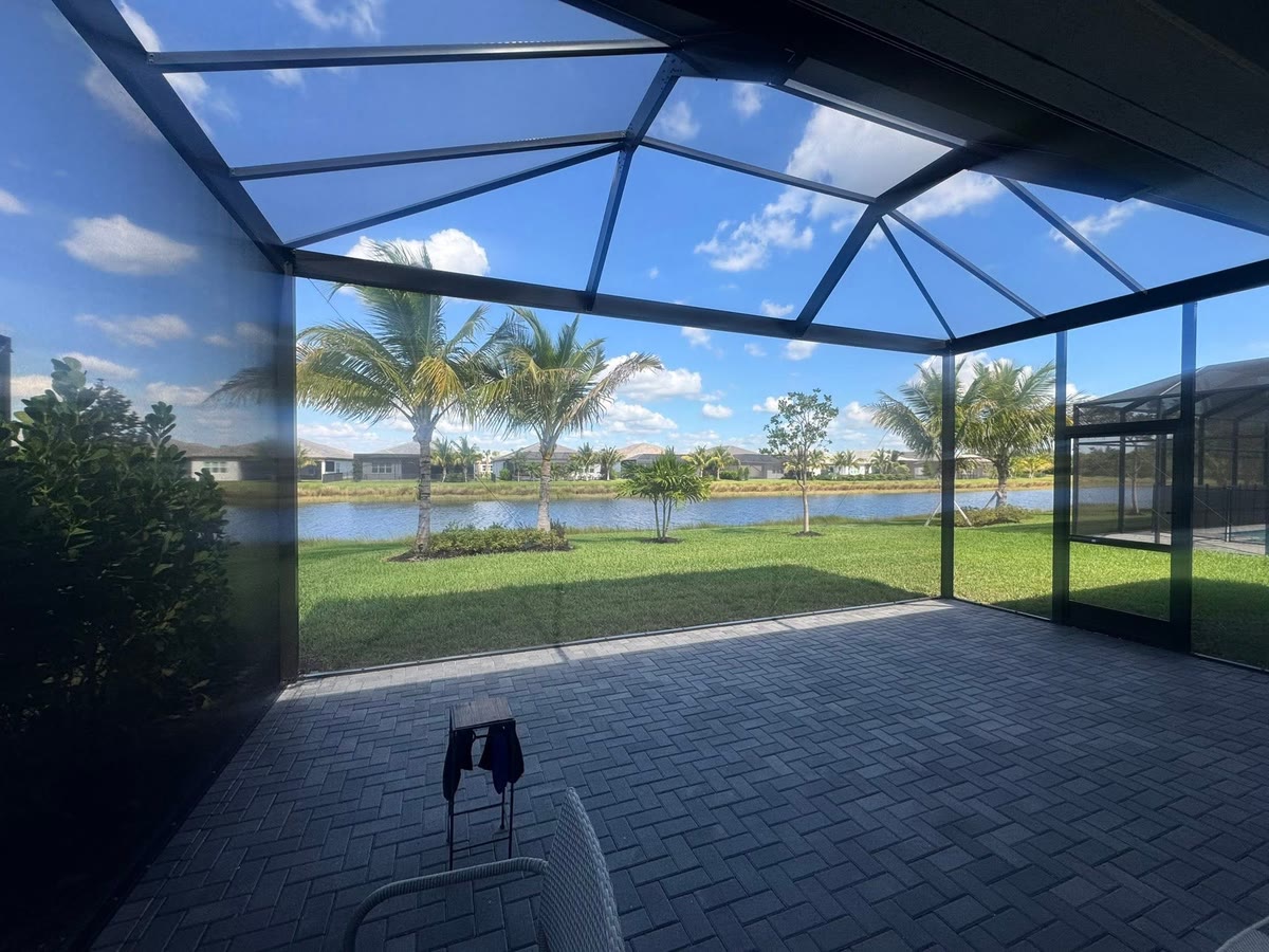 Inside a large screened lanai on a dark paver floor, looking out to a lake.