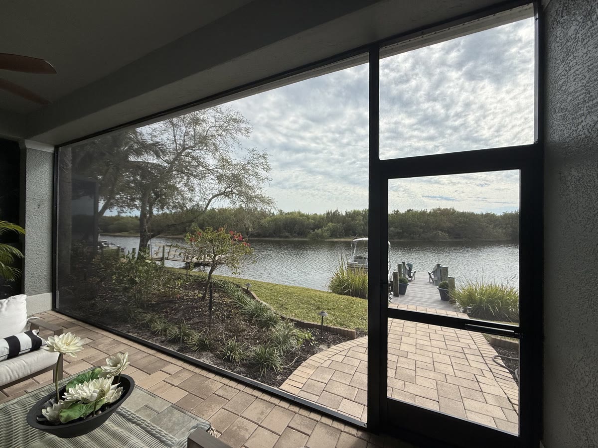 Inside a bronze screen room with a screen door, a lake beyond the lawn.