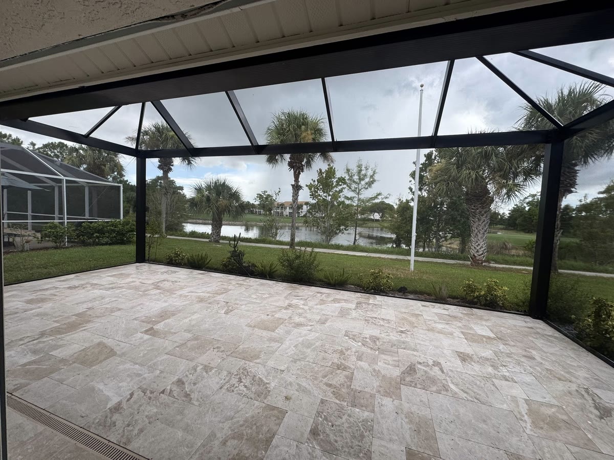 Inside a screened lanai on a pale deck, a pond and palms beyond.