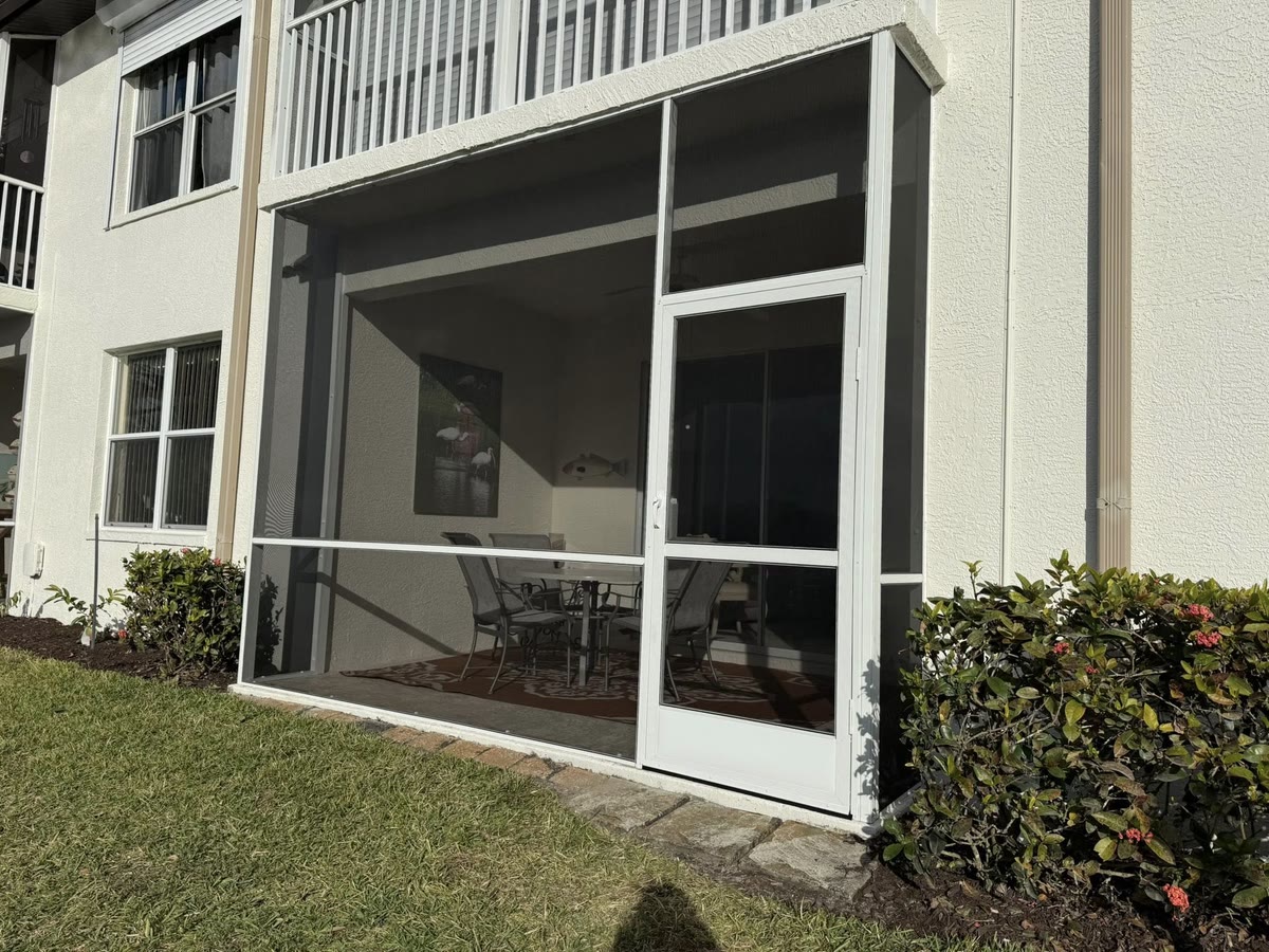 A white screen room with a screen door under a second-floor balcony.