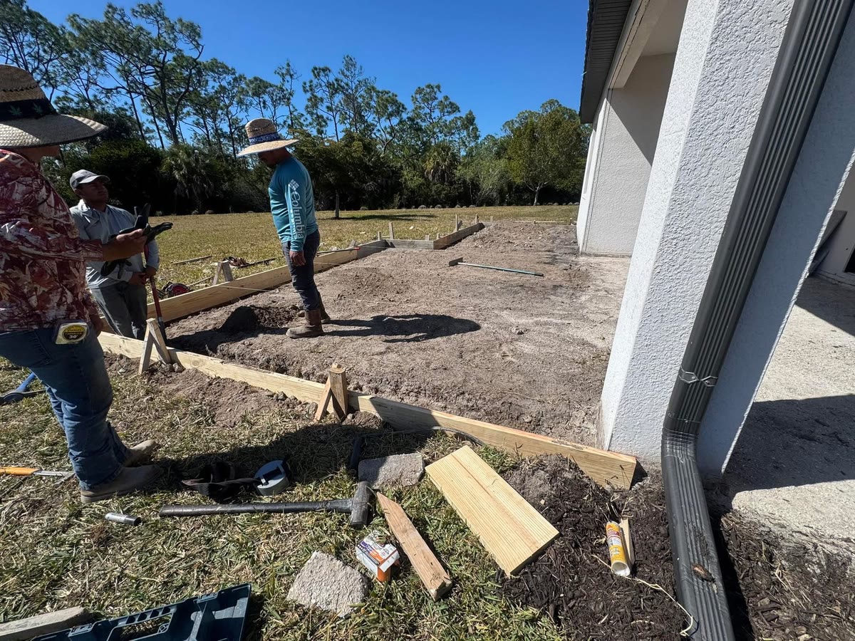 The crew setting the wooden forms for a new slab beside a house.