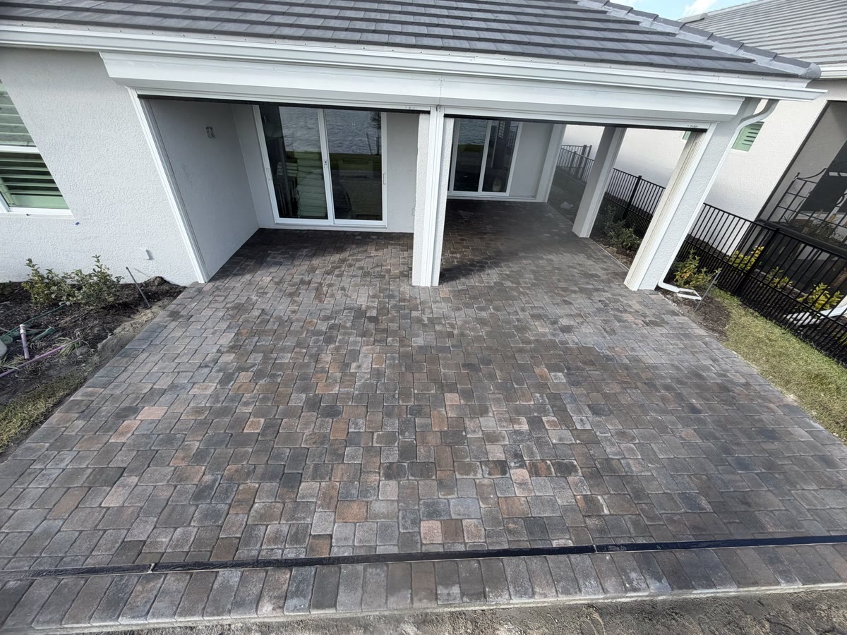 A new paver patio under a white covered lanai at the back of a house.